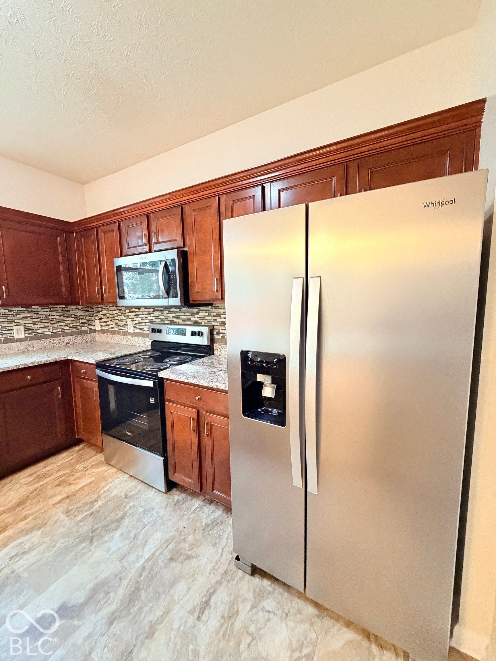 Kitchen featuring stained wood cabinetry, stone-finish countertops, multi-tonal tile backsplash, and stainless steel appliances