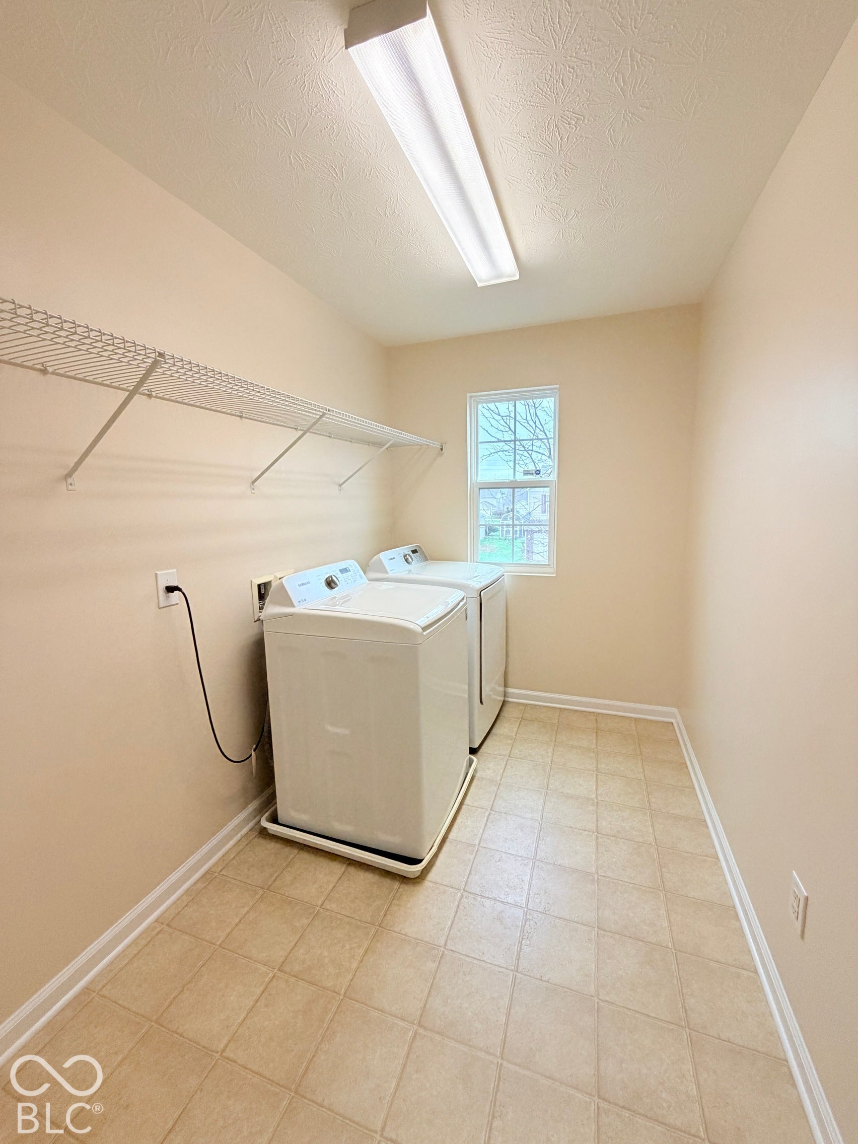 Utility space featuring neutral walls, tile-patterned flooring, a single-hung window, and wall-mounted wire shelving