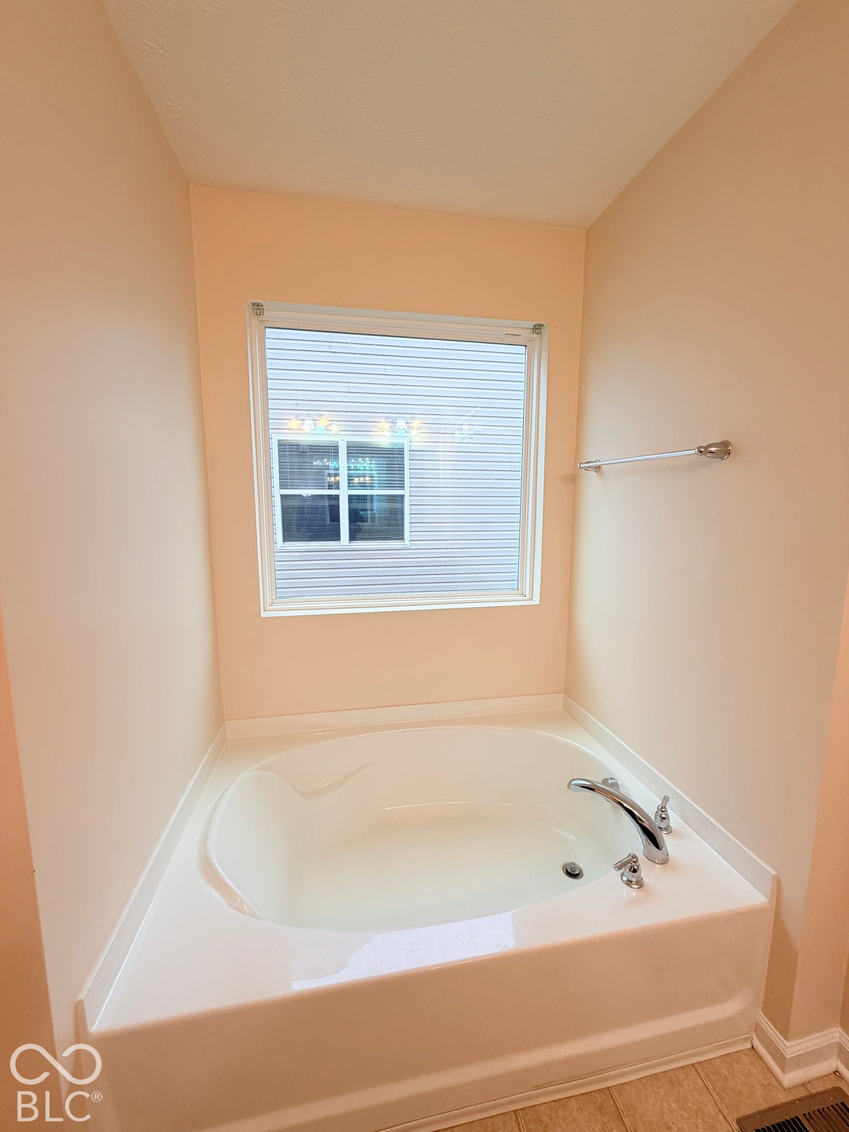 Soaking tub featuring a tiled deck, brushed-nickel faucet, and a wall-mounted towel bar