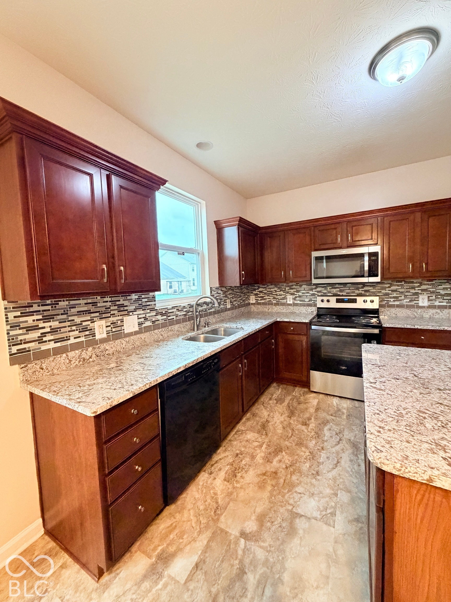 Kitchen featuring stained wood cabinetry, stone-patterned countertops, a decorative mosaic tile backsplash, stainless steel appliances, and tile flooring