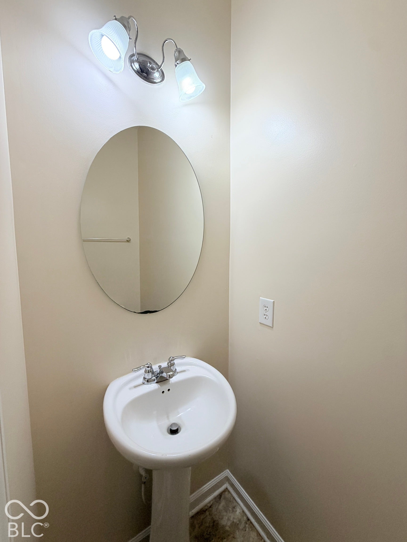 Pedestal sink with dual-handle faucet, oval wall-mounted mirror, and dual-shade vanity light fixture