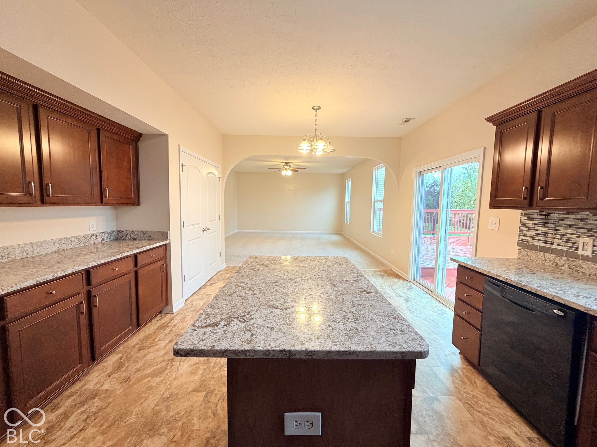 Kitchen featuring dark-finish cabinetry, stone-style countertops, a central island, a multi-colored tile backsplash, and a sliding glass door
