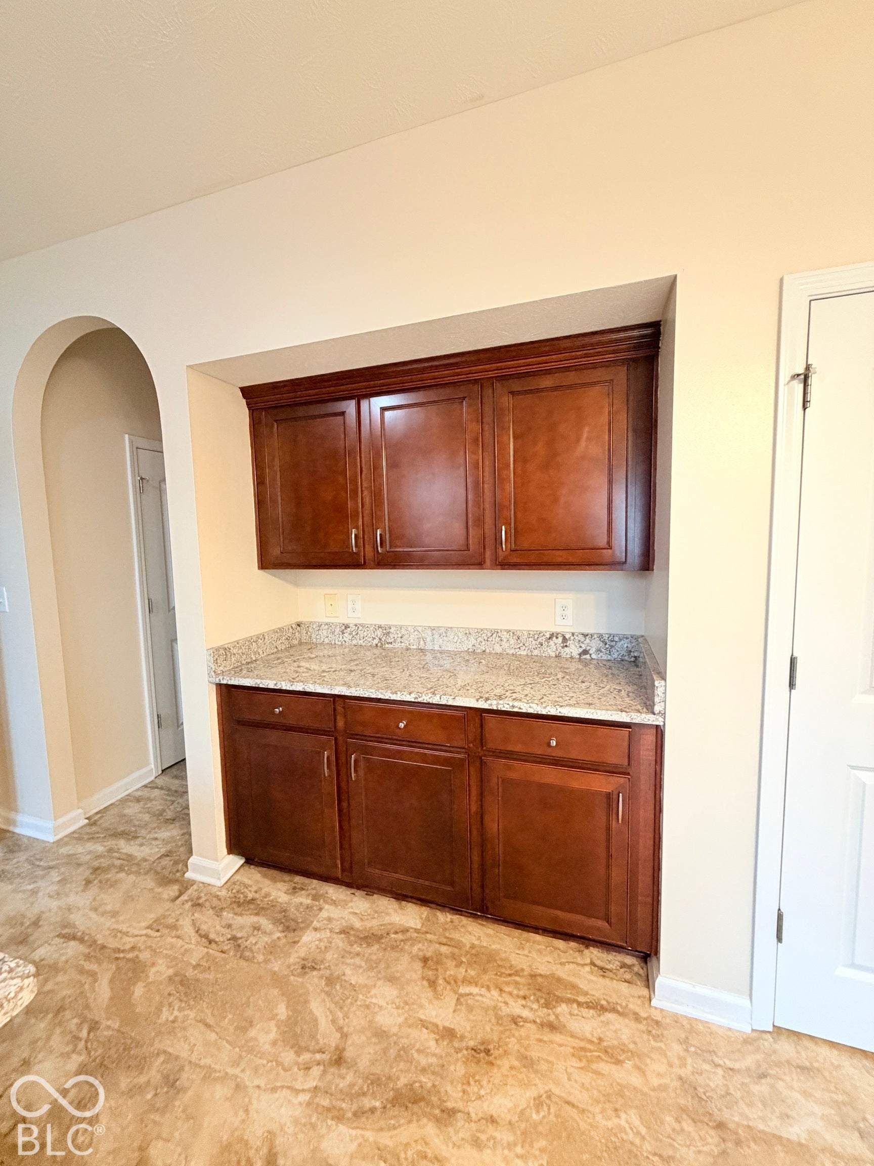 Built-in cabinetry featuring wood-finish lower and upper cabinets, light-toned stone-patterned countertops, and an arched architectural opening