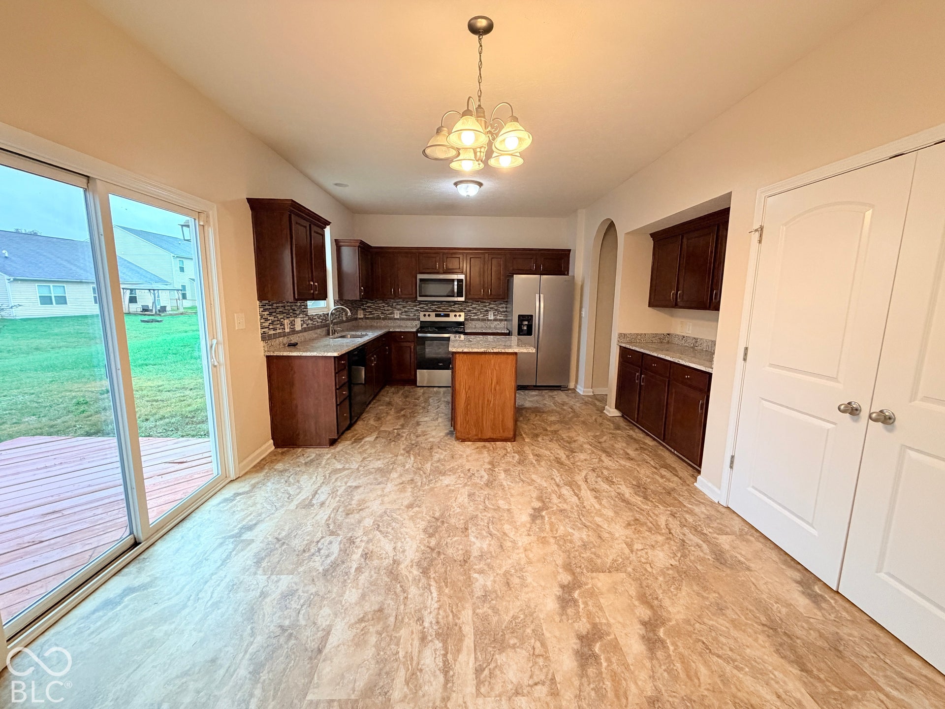 Kitchen featuring stained wood cabinetry, stone-finish countertops, a center island, stainless steel appliances, and sliding glass doors