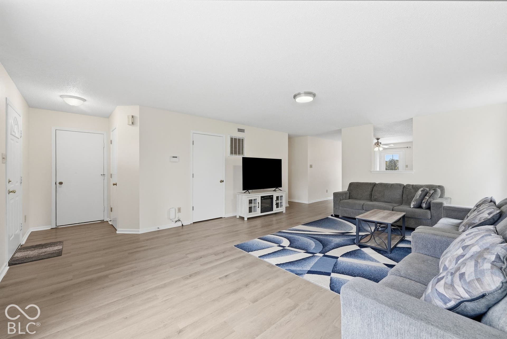 Open-concept living space featuring wood-finish flooring, neutral wall paint, and a pass-through window cutout