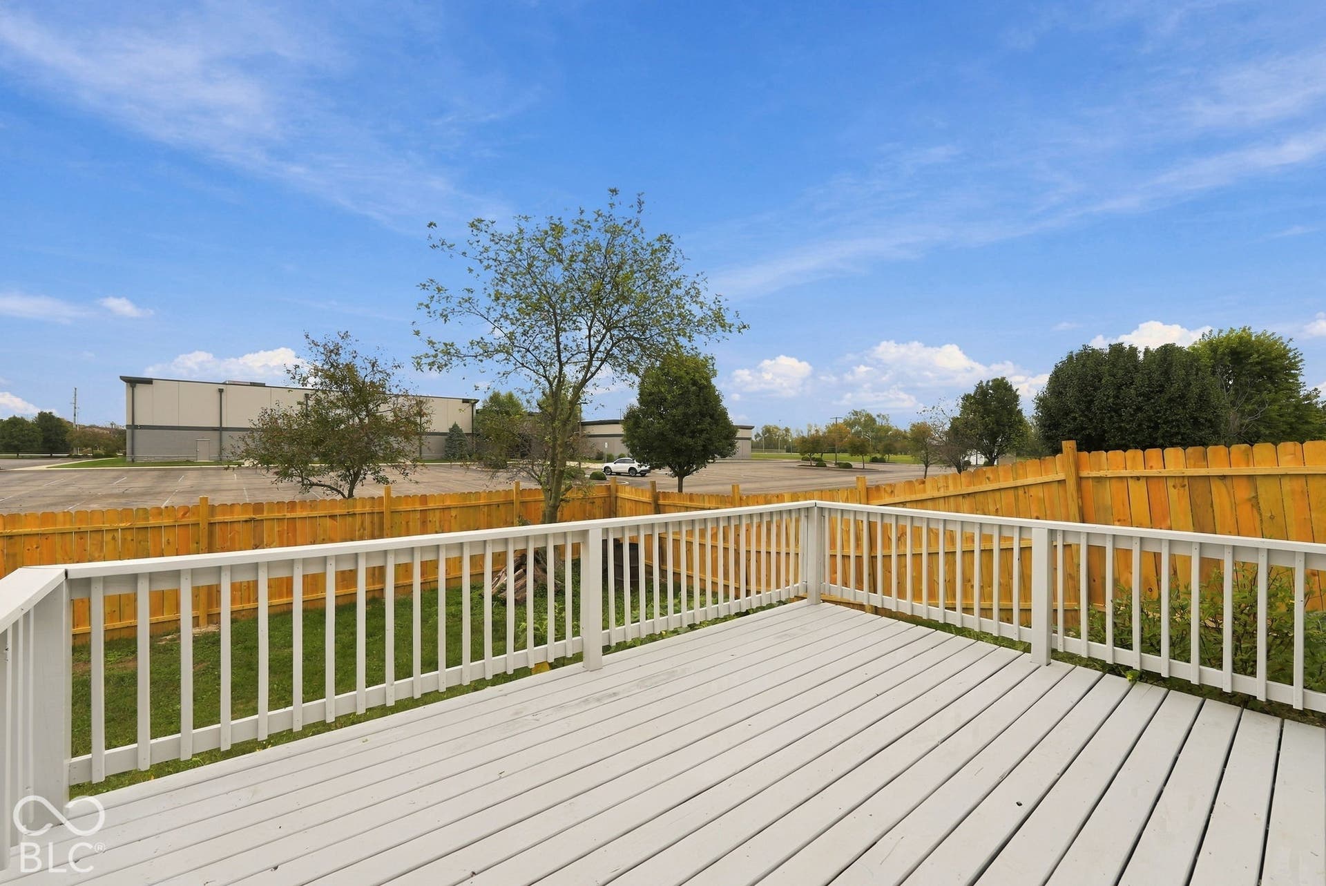 Elevated deck featuring painted wood-finish decking and white wood balustrades, enclosed by a wood privacy fence