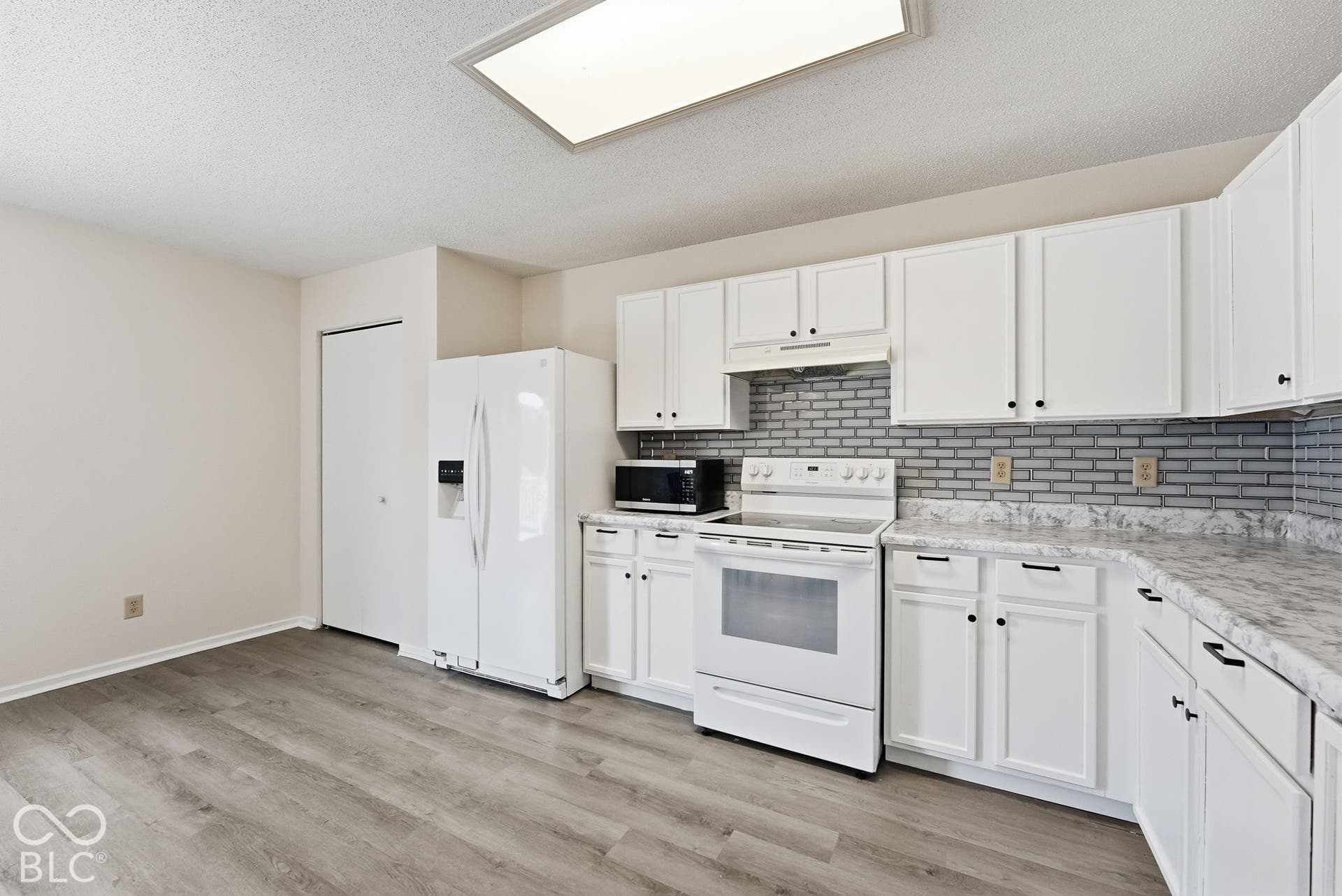 Kitchen featuring white cabinetry, stone-patterned laminate countertops, grey brick-style backsplash, integrated range hood, and wood-finish flooring