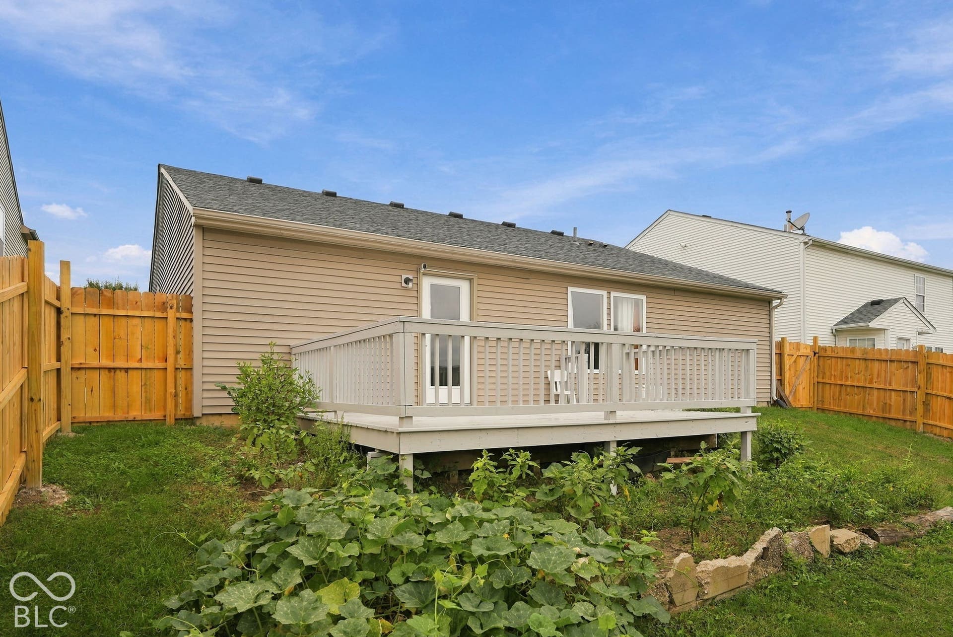 Exterior rear elevation featuring a raised wood deck with painted railing, horizontal vinyl siding, asphalt shingle roof, and full wood privacy fencing