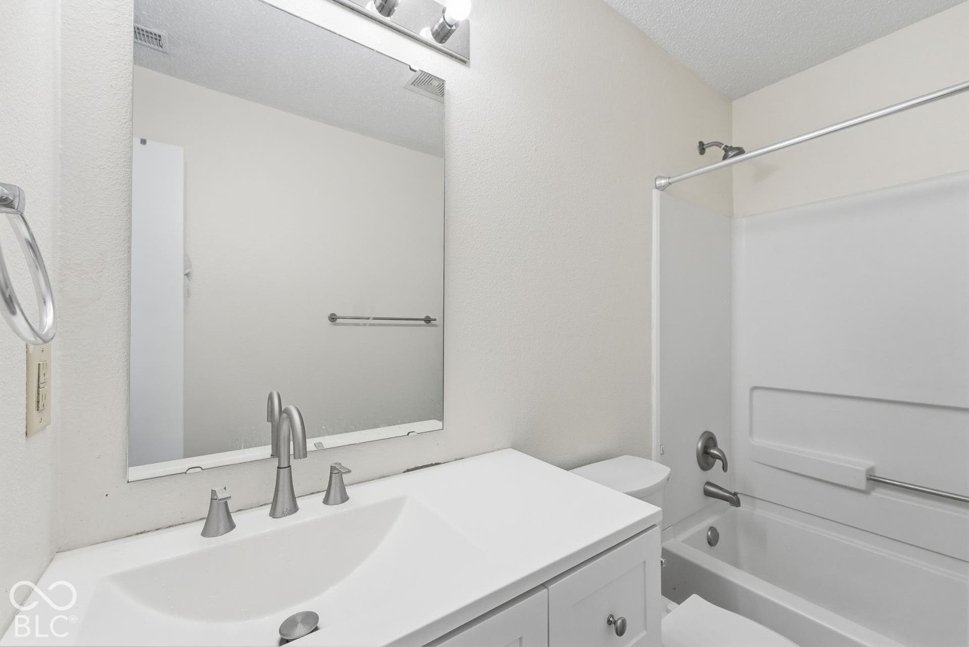 Bathroom featuring a white vanity with an integrated sink, polished metal faucet, large frameless mirror, and a combination tub and shower with a white surround
