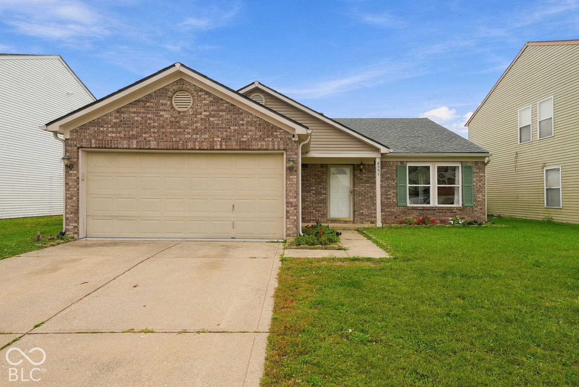Brick and vinyl siding exterior featuring a front-facing attached garage, concrete driveway, and shuttered windows