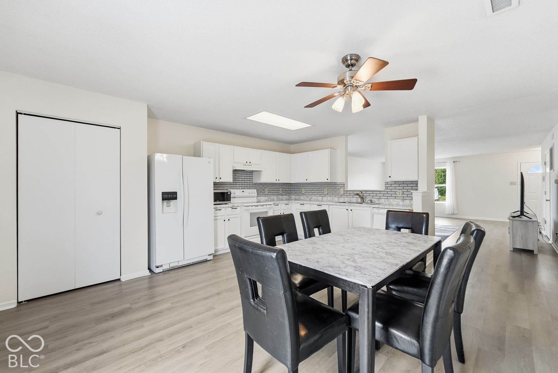 Kitchen featuring white cabinetry, subway tile backsplash, skylight, ceiling fan, and wood-finish flooring