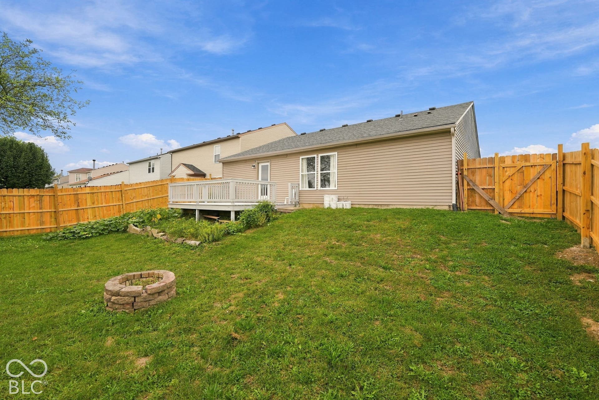 Rear exterior featuring vinyl siding, an elevated wood deck, a fenced backyard, and a stone-style fire pit