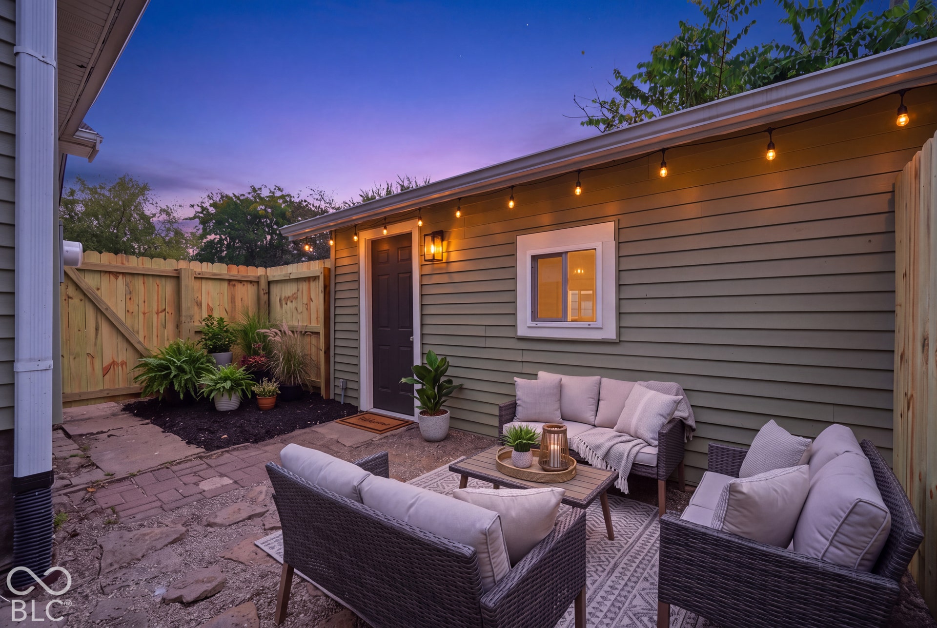 Private courtyard featuring horizontal siding, flagstone hardscaping, a raised wood fence, and mounted string lighting