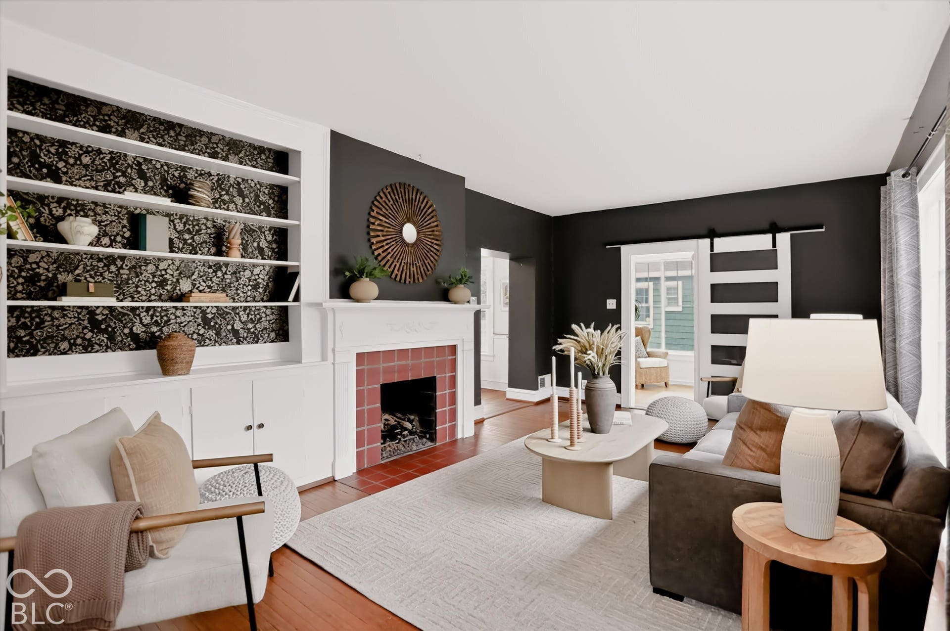 Built-in shelving with patterned backing, fireplace with red tile surround, white mantelpiece, wood-finish flooring, and white paneled sliding door with matte black hardware