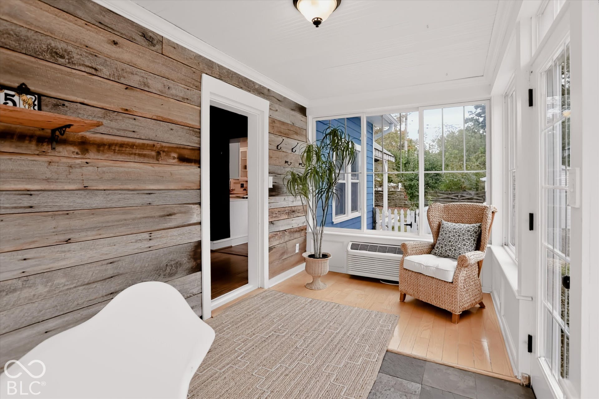 Enclosed sunroom featuring rustic horizontal wood-plank walls, expansive multi-pane windows, wood-finish flooring, and a tiled threshold