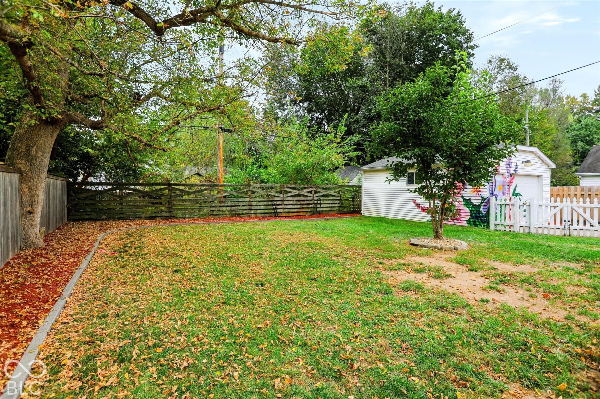 Backyard featuring a grass lawn, detached garage, perimeter wood fencing, and mature trees