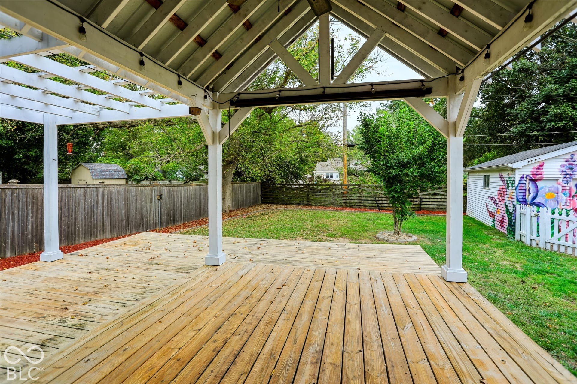 Covered wooden patio featuring a vaulted timber-frame structure, a wooden pergola extension, and a fenced backyard