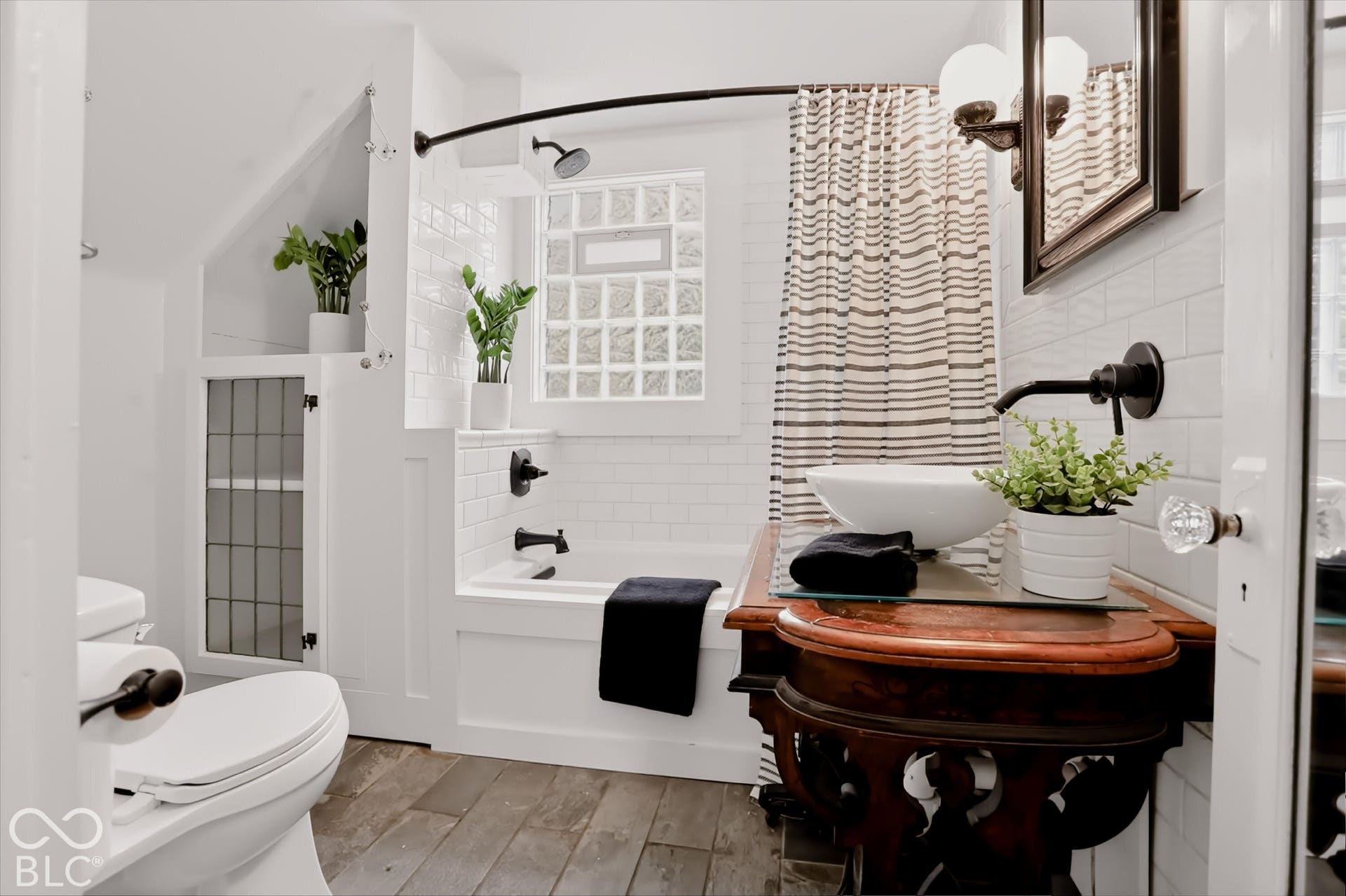 Bathroom featuring a pedestal-style vanity with a glass countertop, white vessel sink, matte black wall-mounted faucet, subway tile surround, and glass block window