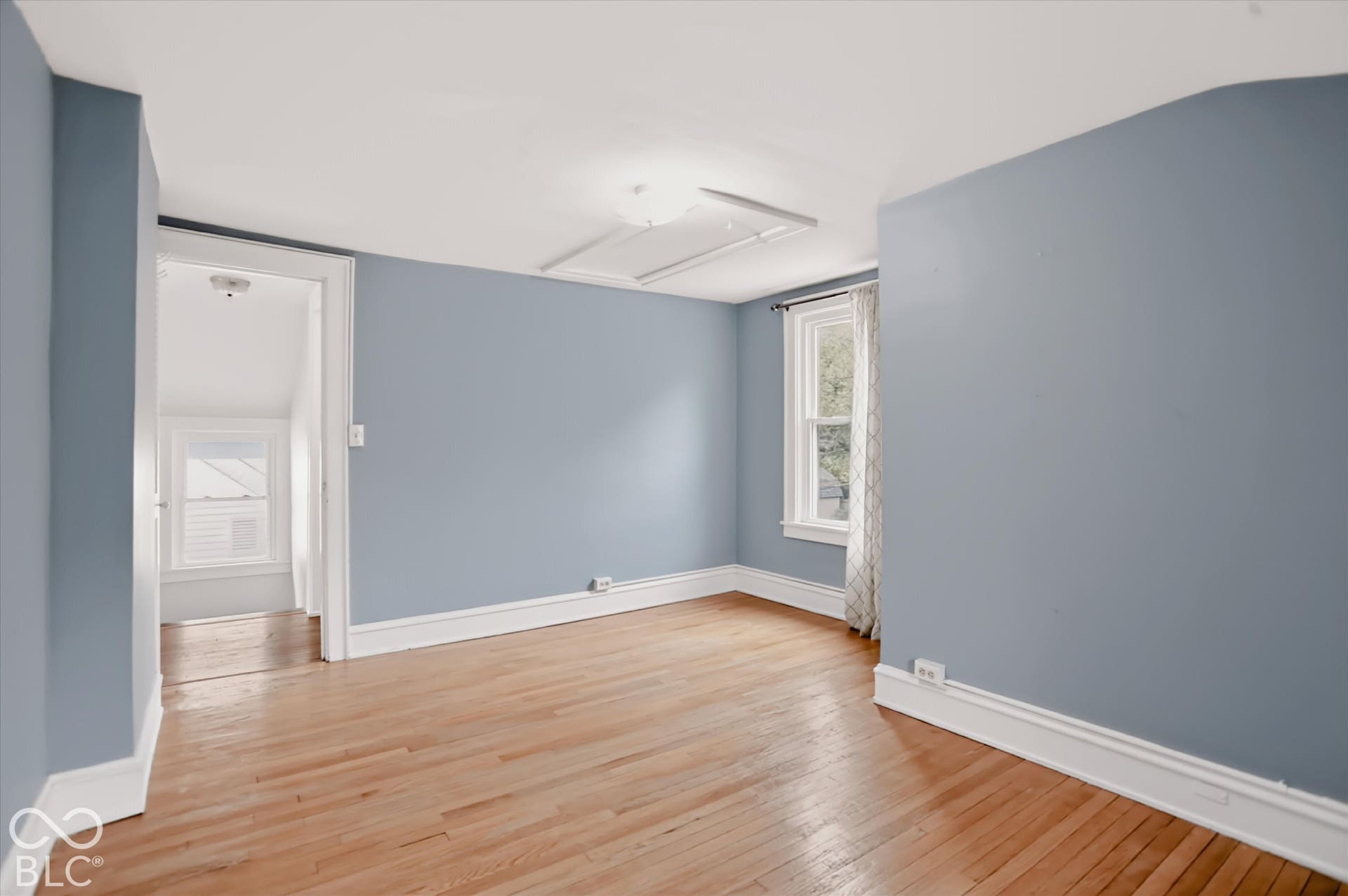 Neutral-toned interior space featuring wood-finish flooring, white window trim, and a ceiling access panel