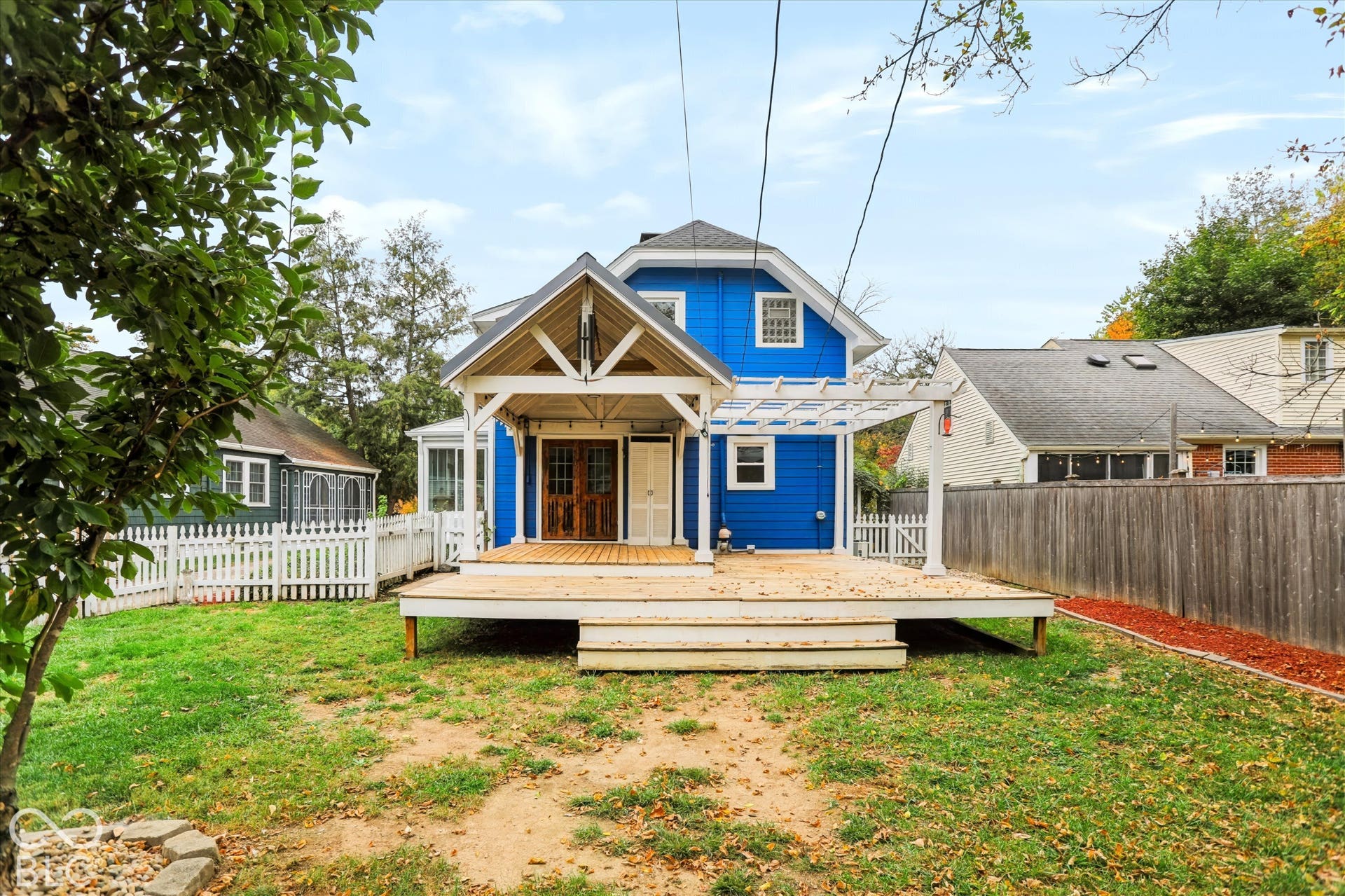 Exterior featuring blue siding, a covered patio with exposed beam trusses, an attached pergola, wood decking, and white picket fencing