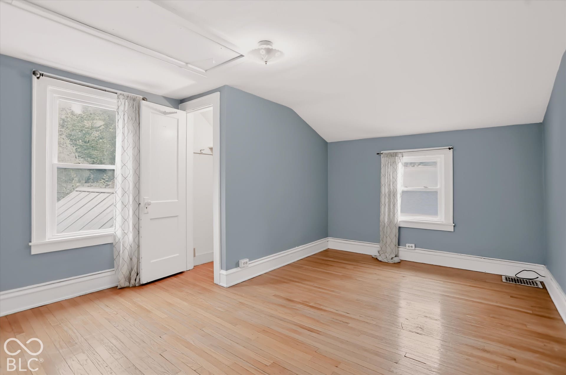 Room featuring wood-finish flooring, vaulted ceiling, dual windows, and built-in closet storage