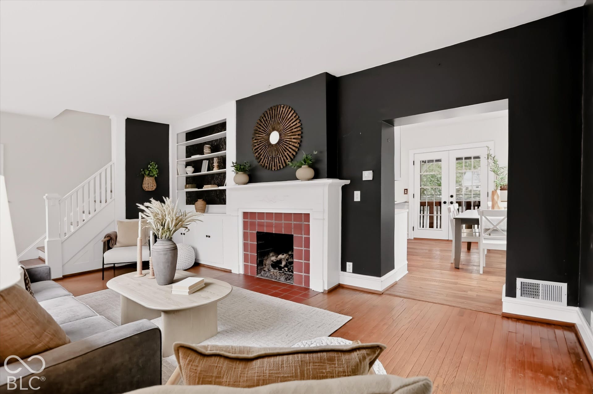 Fireplace with a red tile surround and white mantel, built-in shelving, white staircase railing, and wood-finish flooring