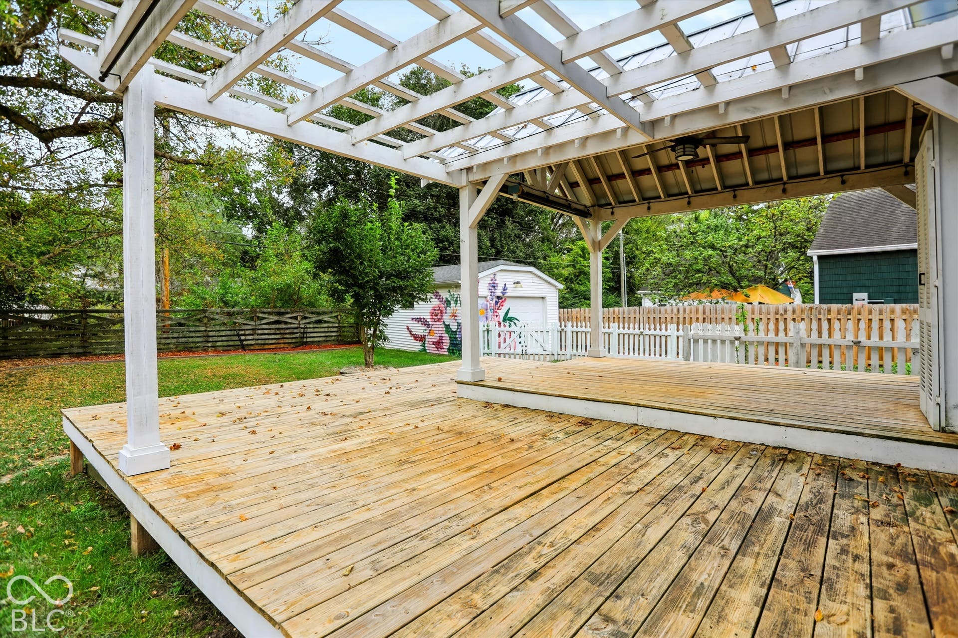 Multi-level wood deck featuring a white pergola, covered patio area, and an attached ceiling fan