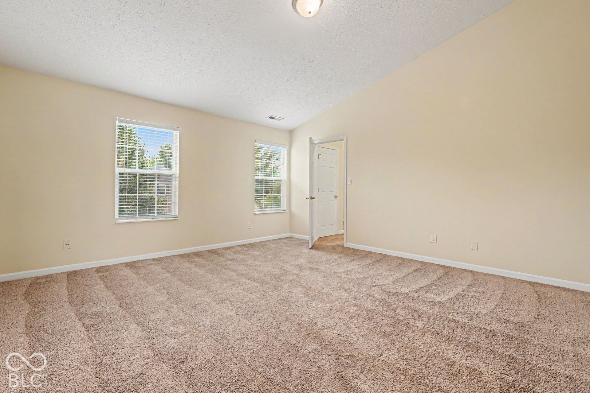 Room featuring vaulted ceilings, neutral wall tones, wall-to-wall carpeting, and multiple windows