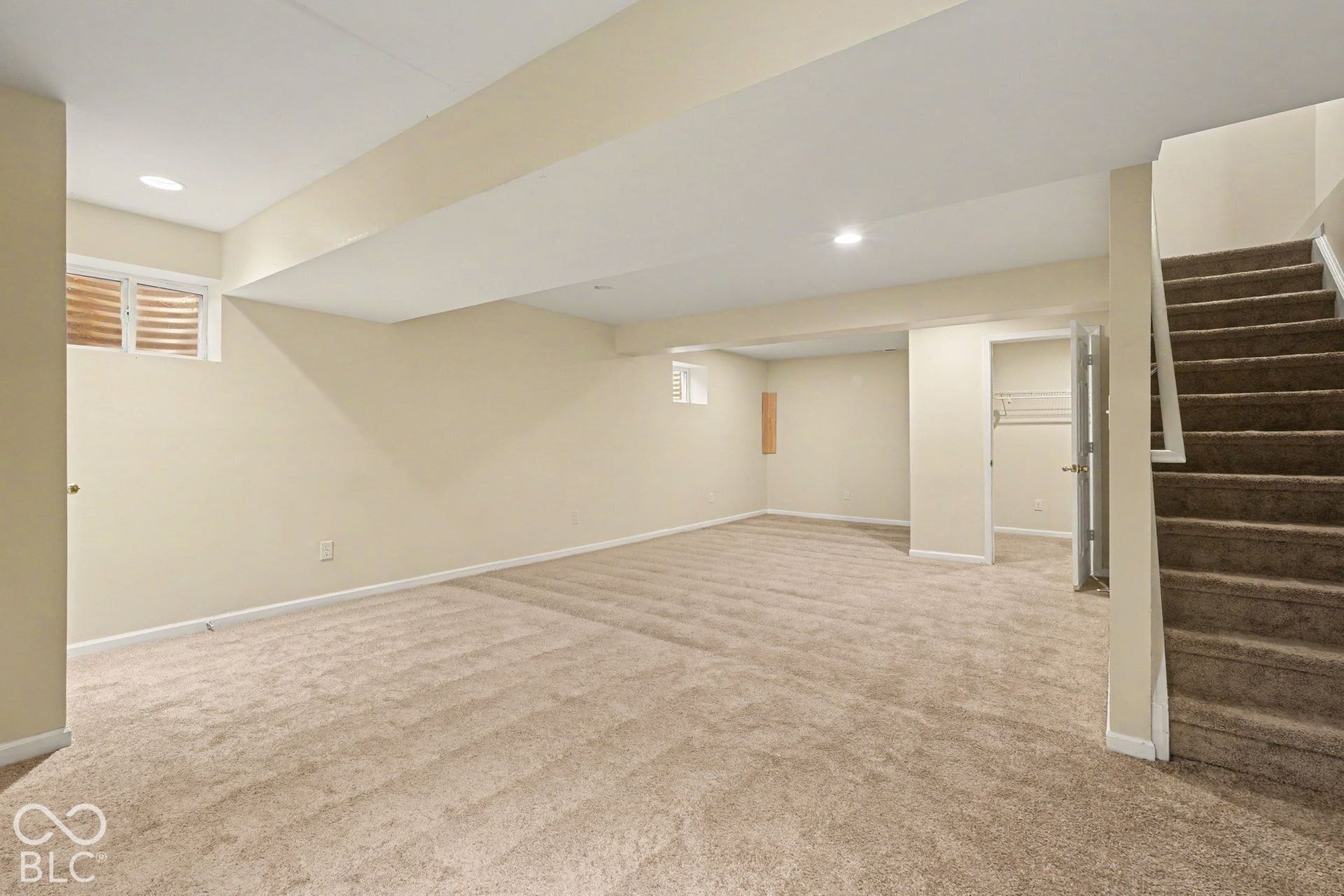 Open-concept room featuring neutral wall-to-wall carpeting, recessed lighting, egress windows, and built-in closet storage