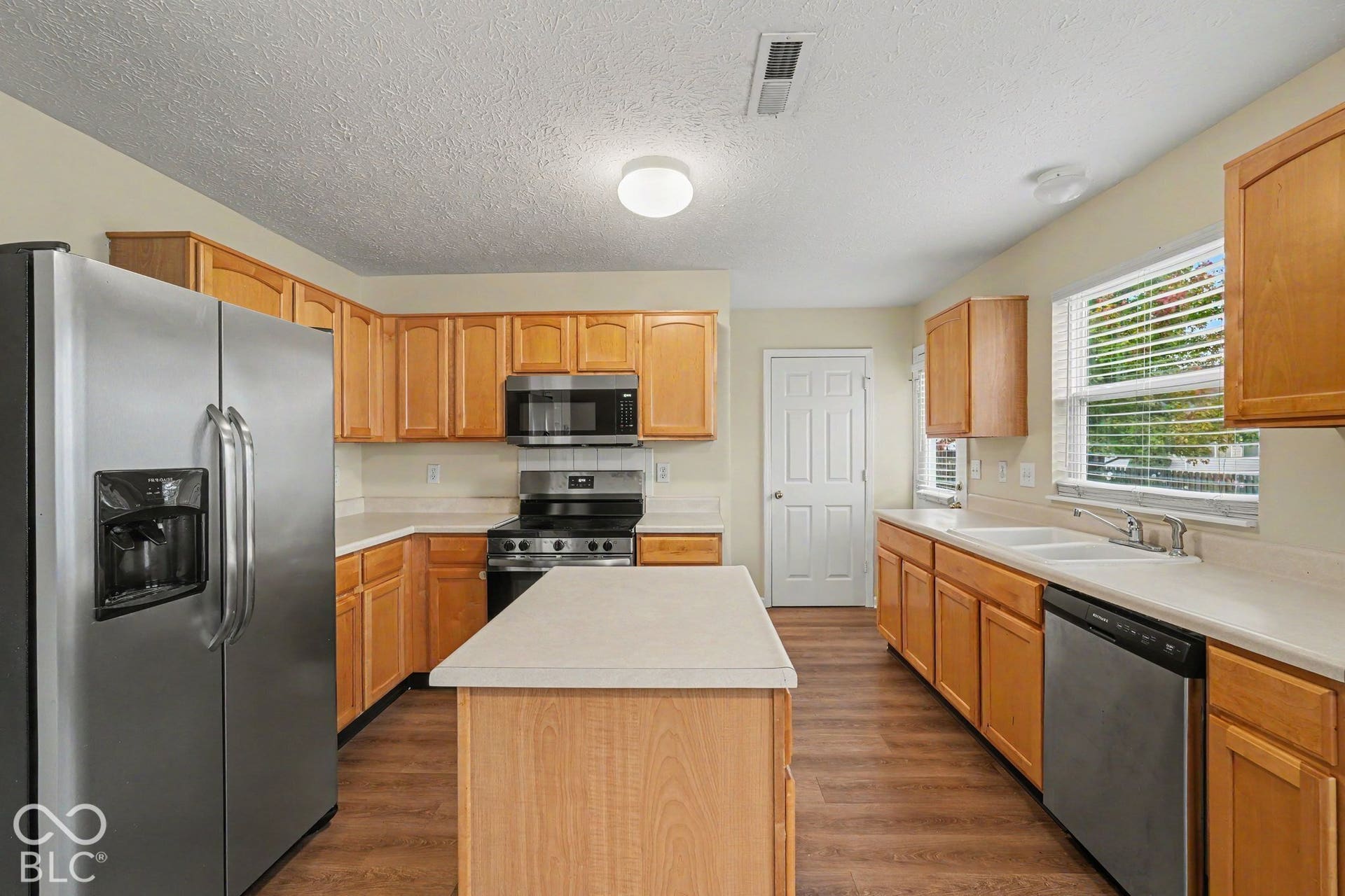 Kitchen featuring wood cabinetry, a central island, stainless steel refrigerator and dishwasher, and wood-finish flooring