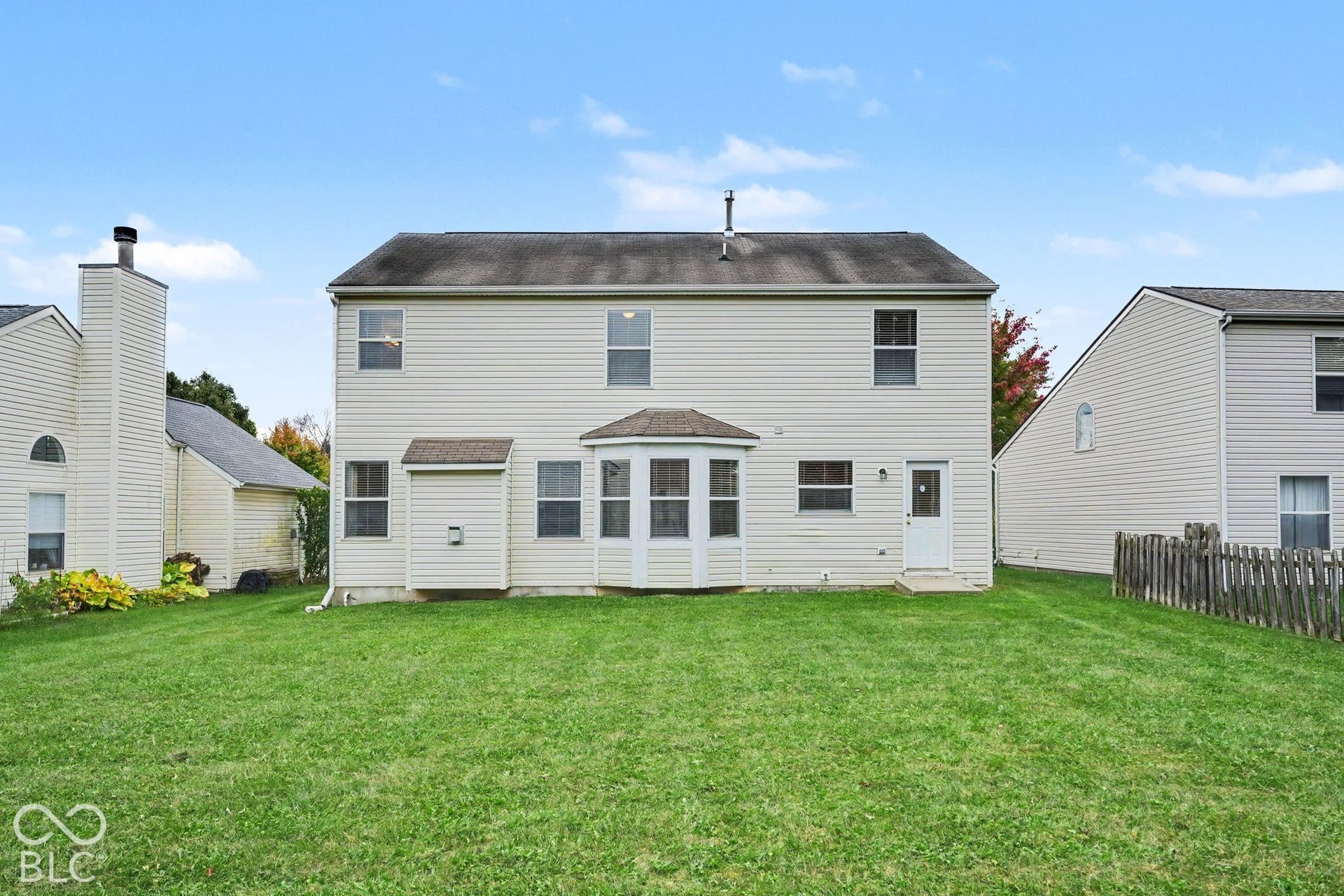 Two-story residence featuring light-colored siding, a rear bay window, a shingle roof, and a fenced-in grassy yard