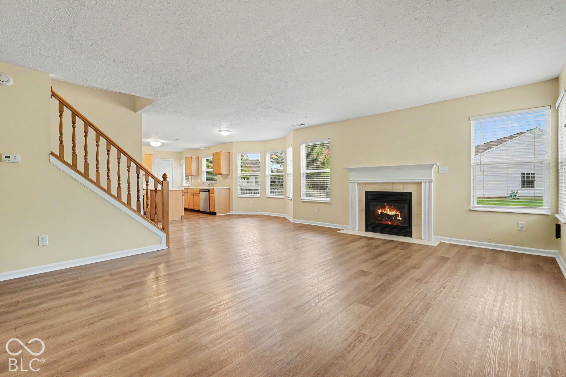 Wood-finish flooring throughout, fireplace with a custom mantle, staircase with wood railings, multiple windows, and built-in kitchen cabinetry