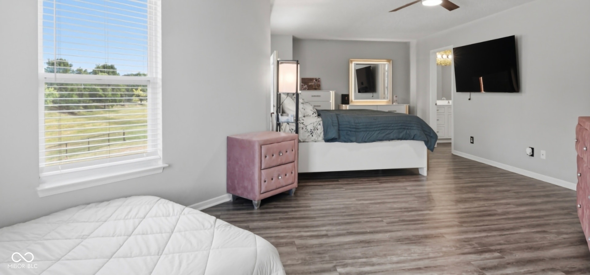 Spacious room featuring wood-finish flooring, a ceiling fan, and a large window with horizontal blinds