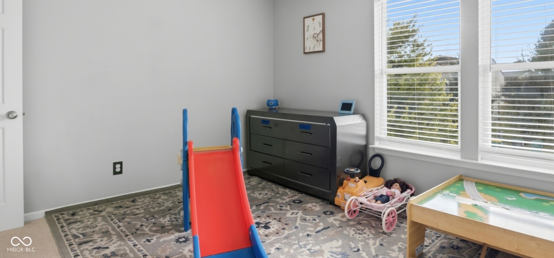Bright room featuring multiple large windows with horizontal blinds, light gray wall paint, and a patterned area rug