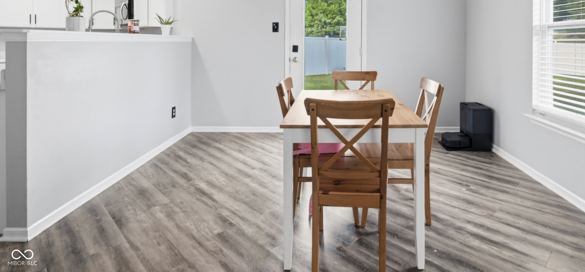 Open-concept dining area featuring wood-finish flooring throughout, a neutral color palette, and abundant natural light from a large window with blinds