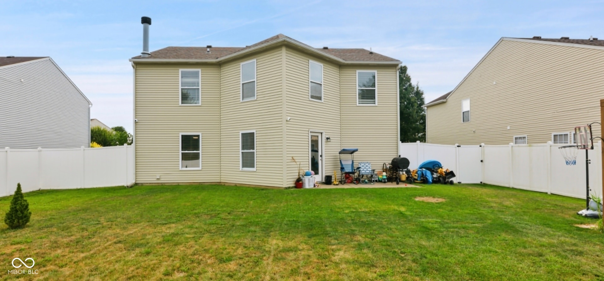 Rear exterior featuring light-colored siding, multiple windows, a ground-level patio, and a white privacy fence encompassing the yard