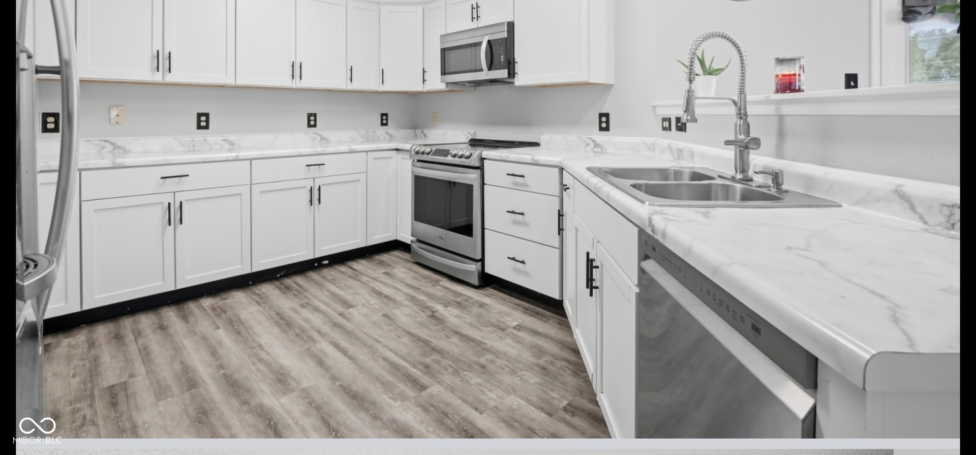 Contemporary kitchen featuring white cabinetry with dark hardware, stainless steel appliances, wood-finish flooring, and light-toned countertops