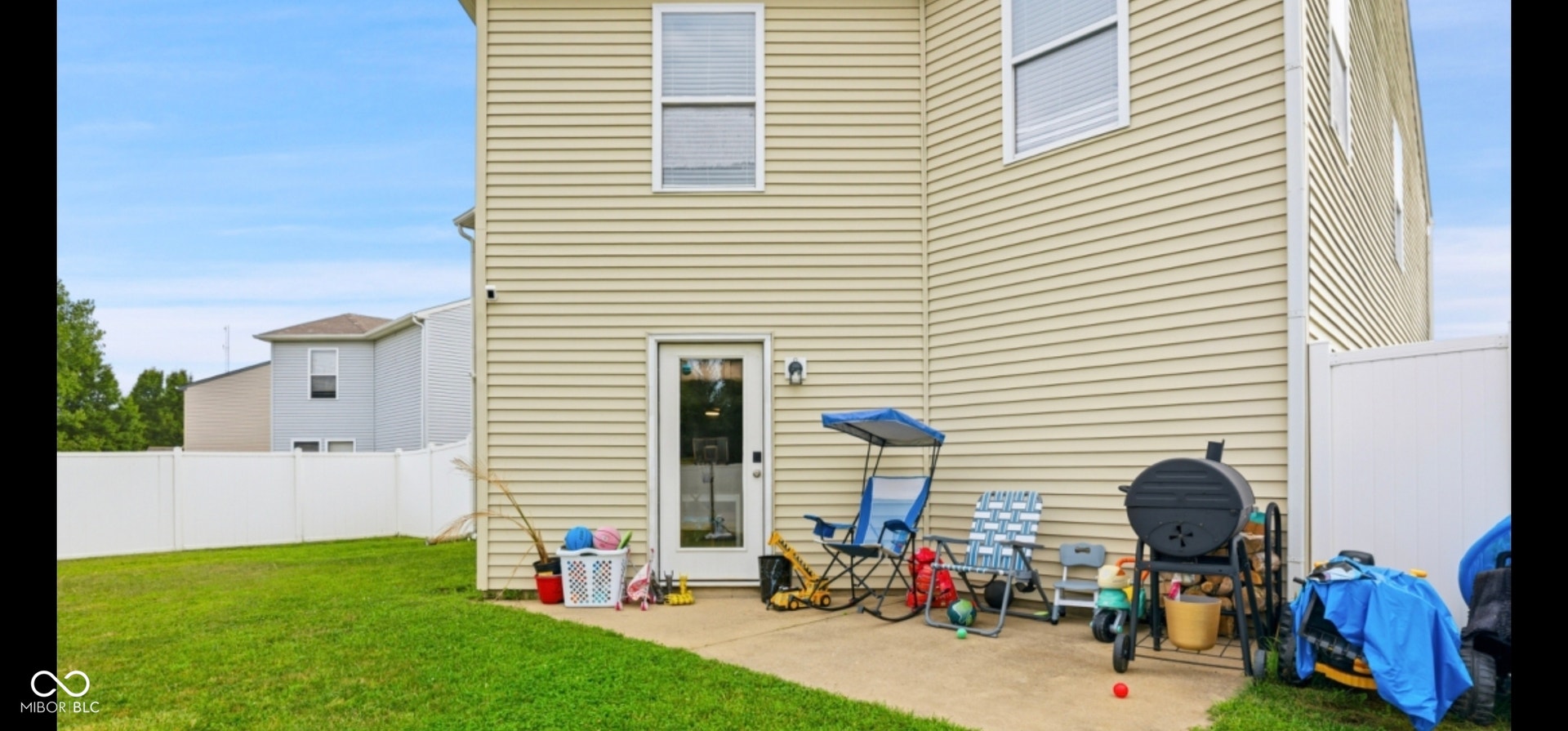 Expansive backyard featuring a manicured lawn, a concrete patio, and a white privacy fence