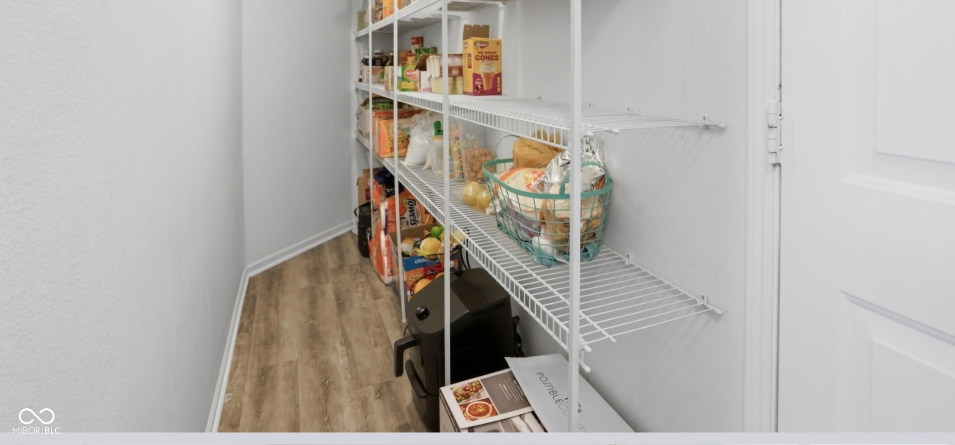 Walk-in pantry featuring extensive wire shelving, wood-finish flooring, and white baseboards