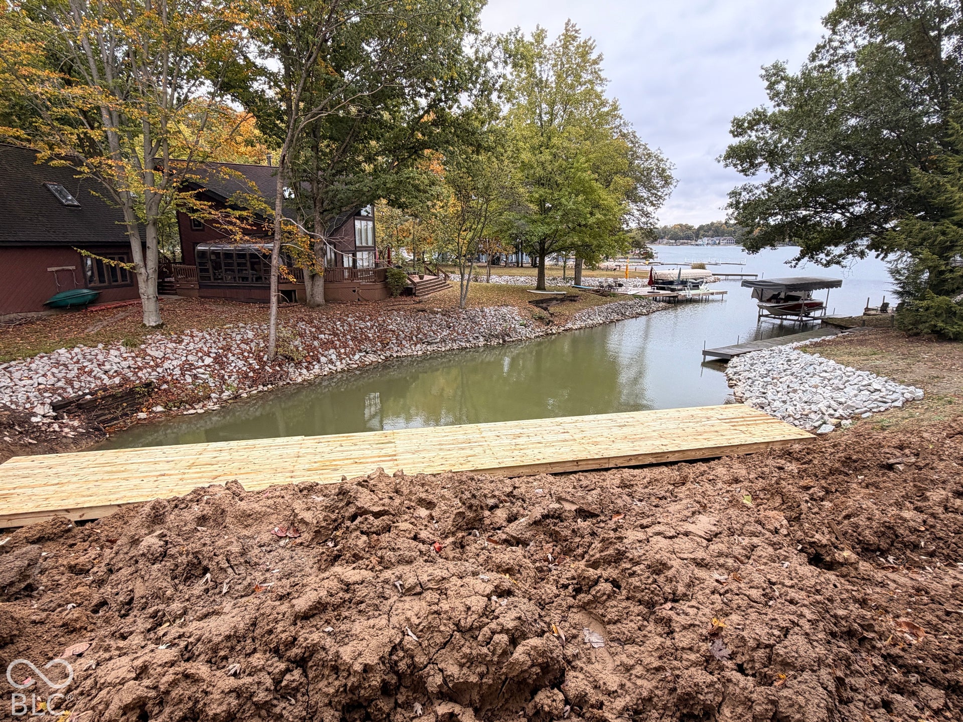 Waterfront property featuring a wood dock, stone shoreline stabilization, and mature trees