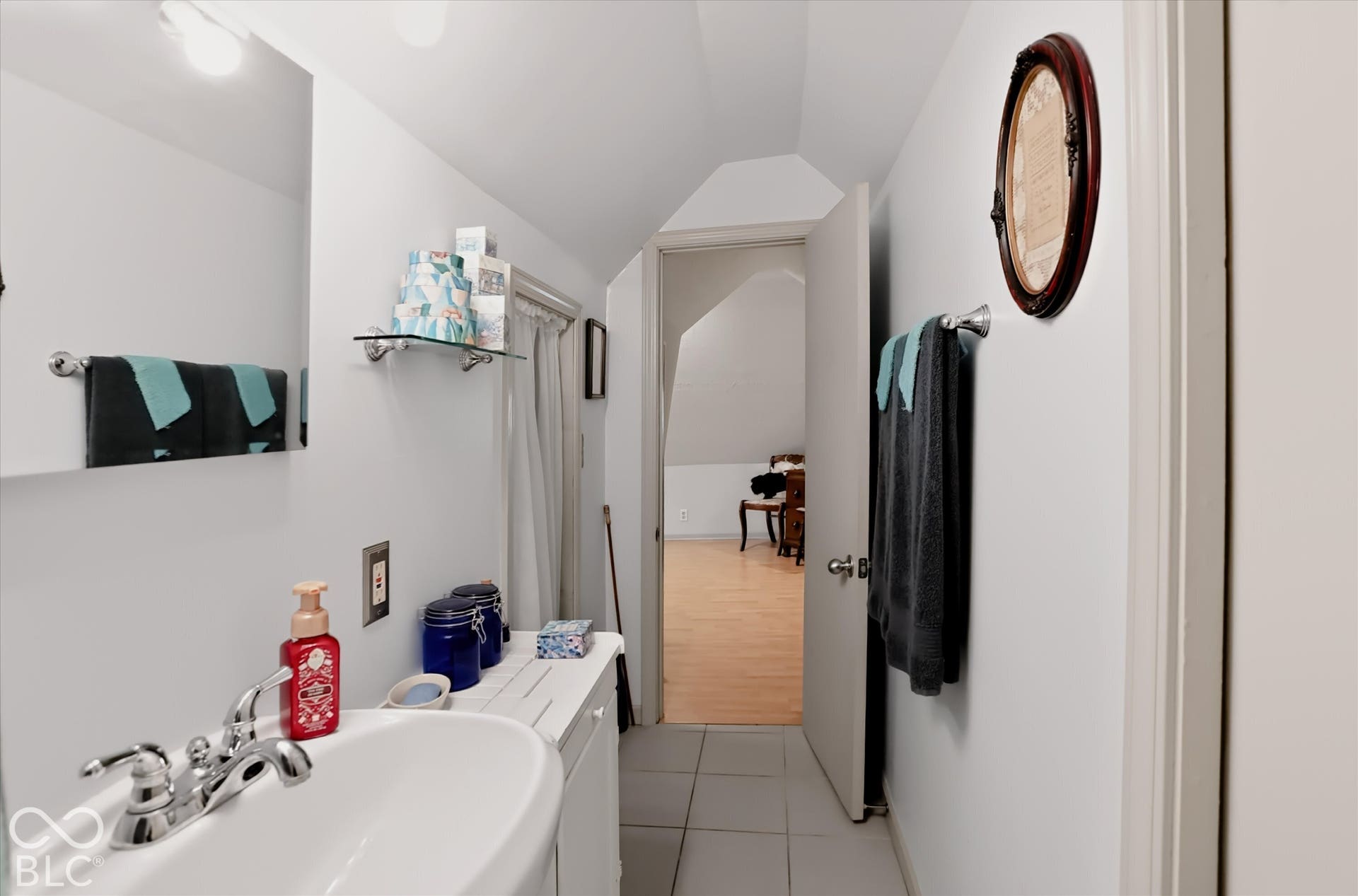 304 W 4th Street, Greenfield, IN 46140 Bathroom featuring a wall-mounted rectangular mirror, vanity with a porcelain sink, polished chrome faucet, glass shelving, and neutral tile flooring