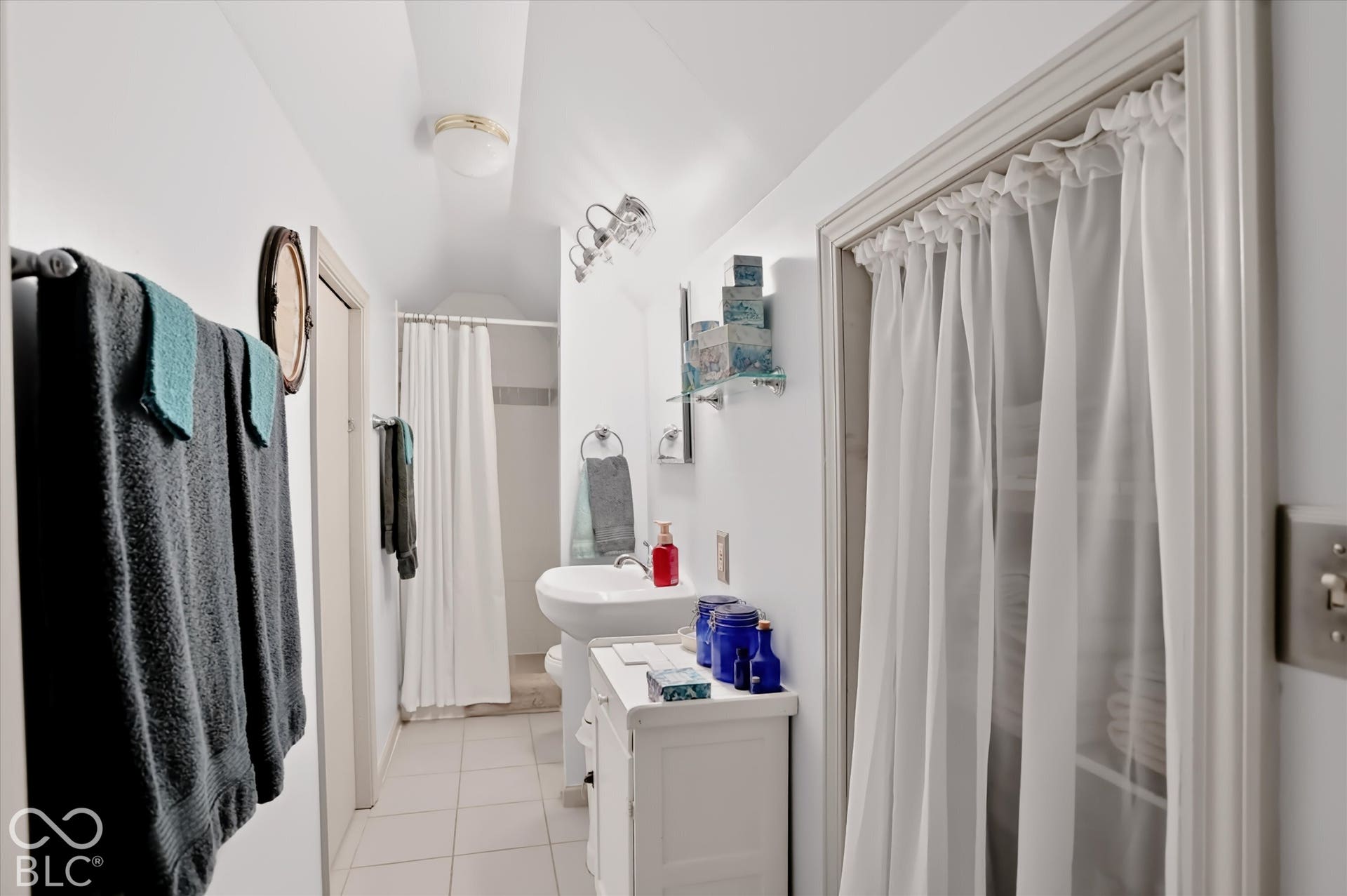 304 W 4th Street, Greenfield, IN 46140 Bathroom featuring a pedestal sink, ceramic tile flooring, built-in shelving with a fabric curtain cover, wall-mounted multi-bulb light fixture, and arched ceiling detail