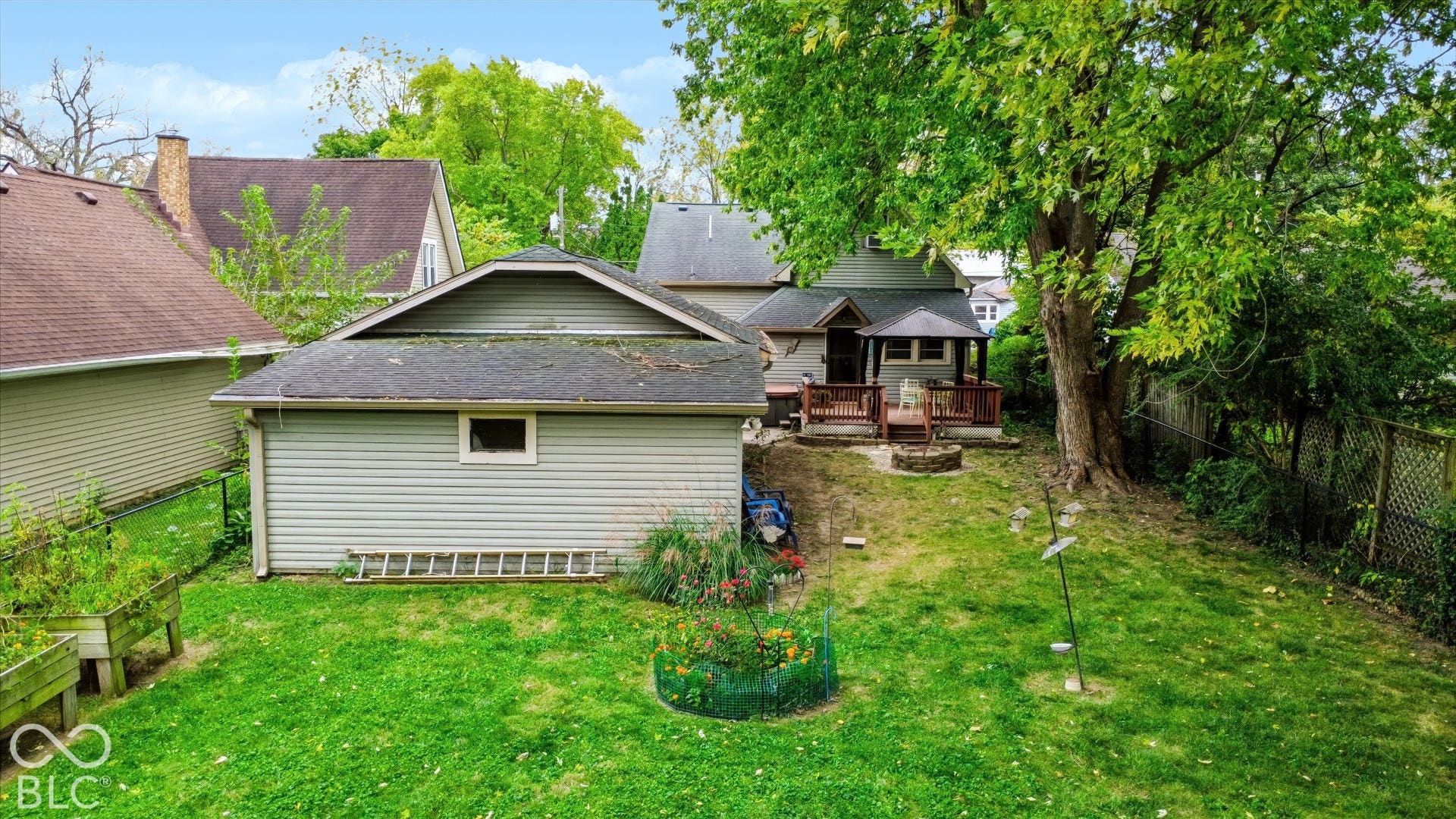 304 W 4th Street, Greenfield, IN 46140 Backyard featuring a detached garage, a wooden deck, a stone fire pit, and mature trees