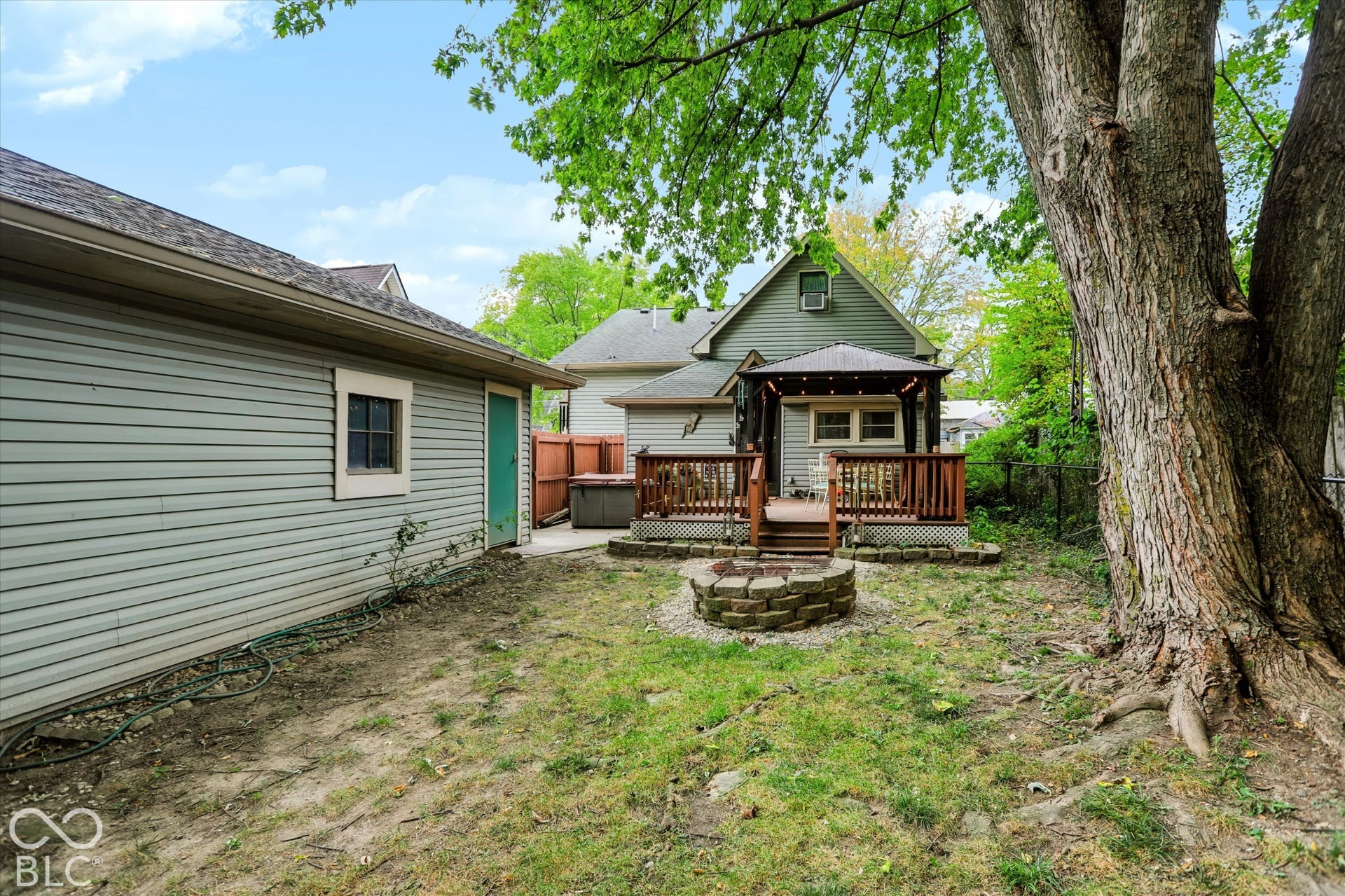 304 W 4th Street, Greenfield, IN 46140 Backyard featuring a raised wooden deck with a built-in pergola, a circular stone fire pit, and a mature tree