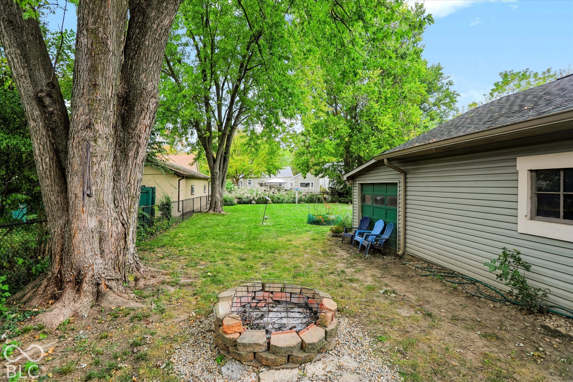 304 W 4th Street, Greenfield, IN 46140 Backyard featuring a stone-lined fire pit, mature trees, chain-link fencing, and a detached garage with horizontal siding