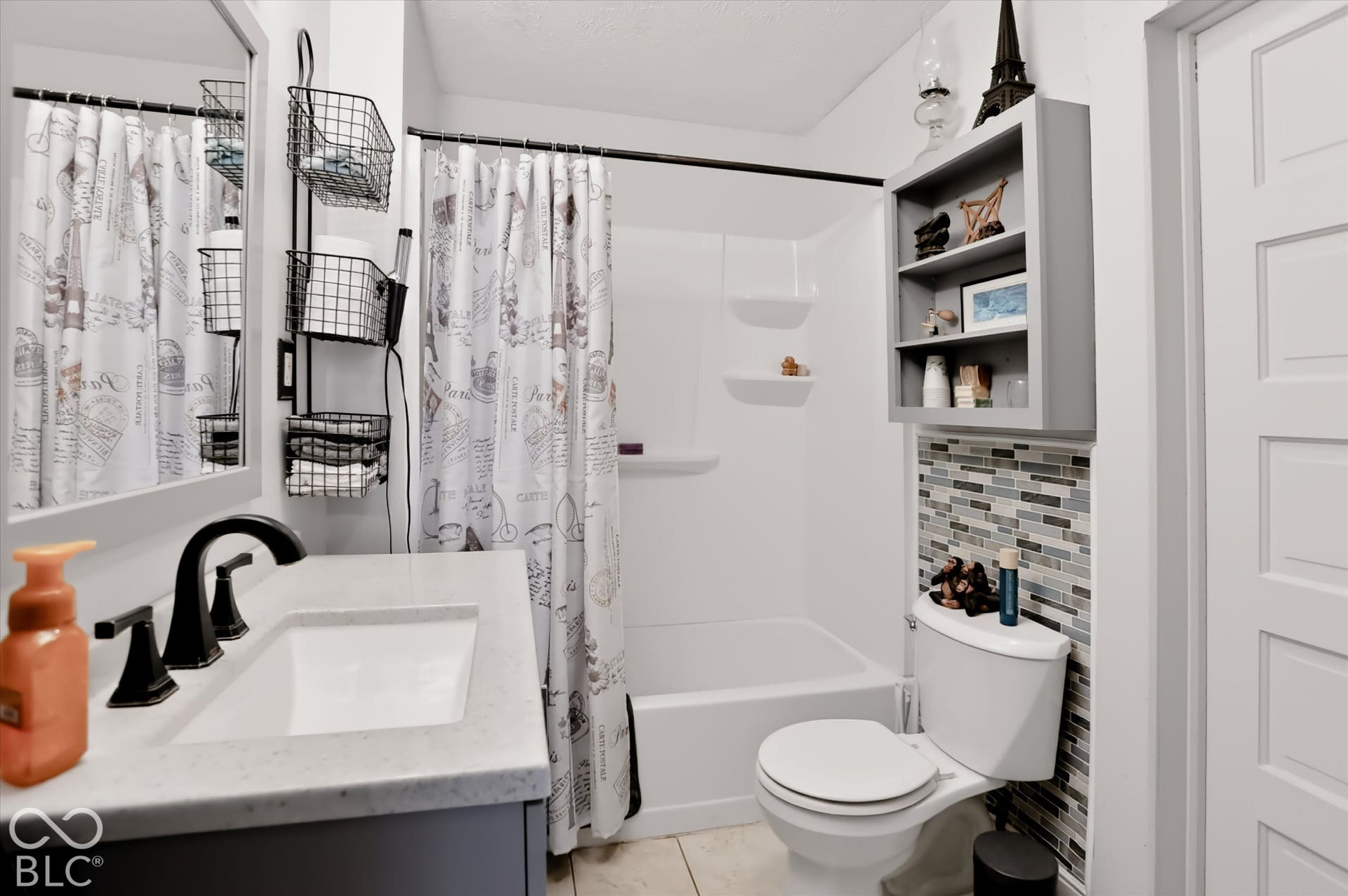 304 W 4th Street, Greenfield, IN 46140 Bathroom featuring a vanity with stone-composite countertop, undermount sink, and matte black faucet, accented by a glass and stone tile backsplash, integrated shower-tub enclosure with built-in shelving, and wall-mounted cabinetry