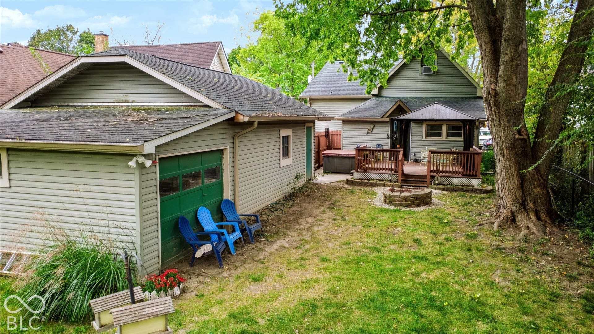 304 W 4th Street, Greenfield, IN 46140 Backyard featuring a detached garage with green paneled door, wood-decked patio, stone fire pit, and mature trees