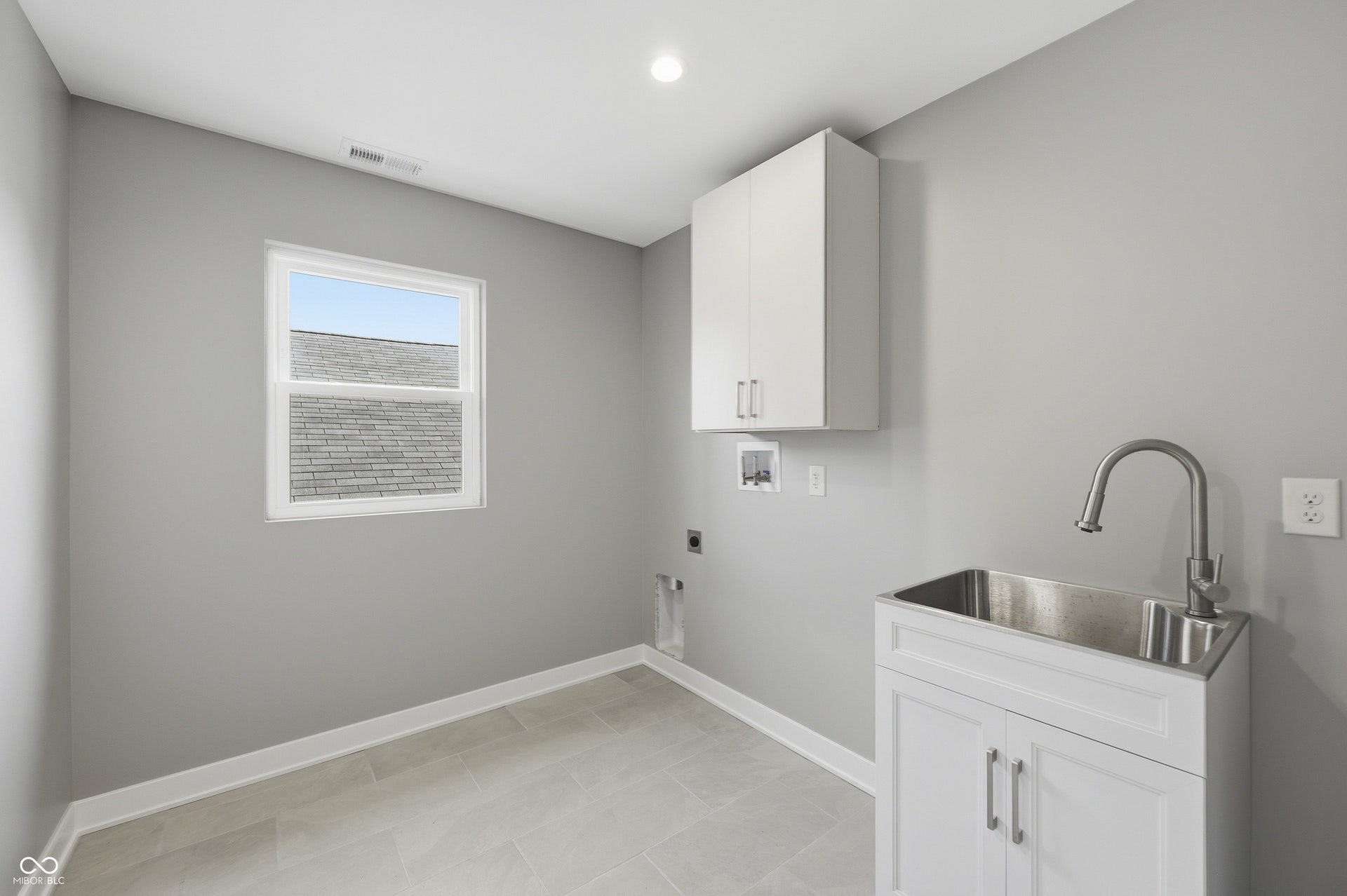 Utility room featuring a stainless steel sink, white shaker-style base cabinetry, and overhead white cabinetry