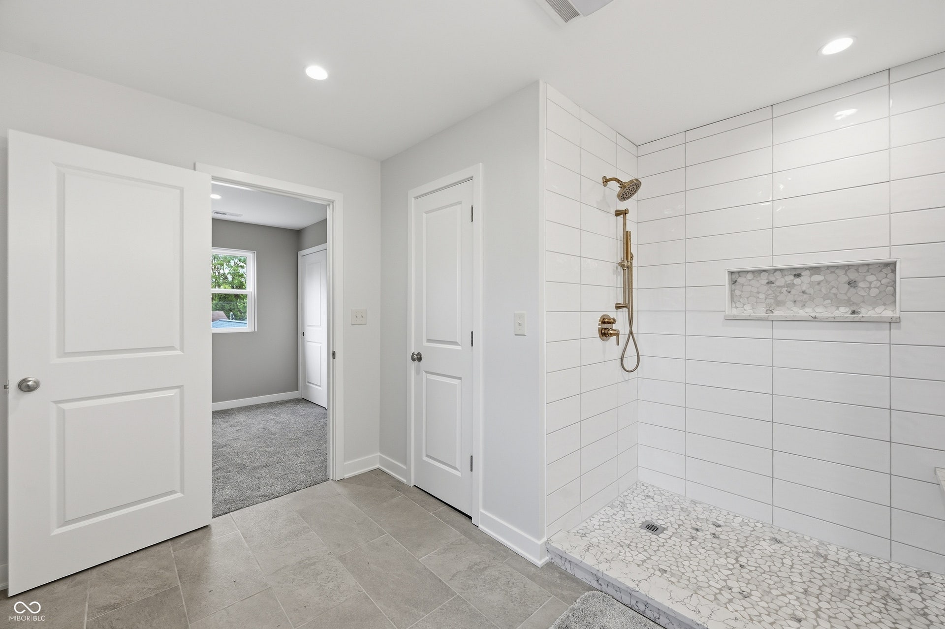 Spacious walk-in shower featuring white subway tile, a recessed niche with pebble tile accent, and a pebble tile shower floor
