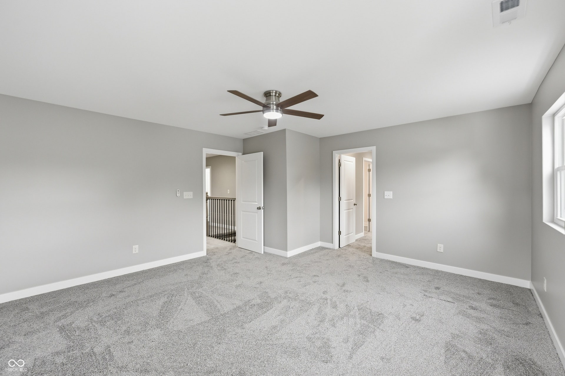 Spacious room featuring neutral grey wall paint, grey carpeting, a ceiling fan with integrated lighting, and white baseboards